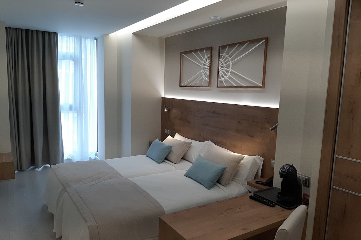 A modern hotel room with a large bed, a wooden headboard, and two wall-mounted abstract art pieces.