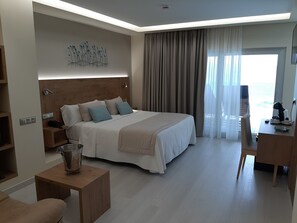 Habitación de hotel moderna con una cama grande, un escritorio, una silla, una mesita de noche y vistas al mar.