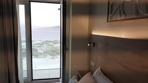 Una habitación de hotel con cama, mesita de noche, un cuadro y vistas al mar a través de una puerta abierta.