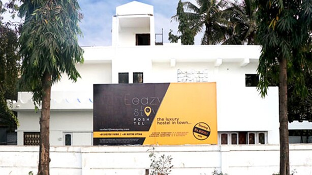 A white building with a large billboard advertising a hostel. - LRH EasyStay 4 (Pune)