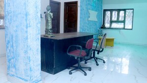 A reception area with a marble floor, a reception desk, two chairs, a statue, and a window with a view of trees. - LRH EasyStay 4 (Pune)