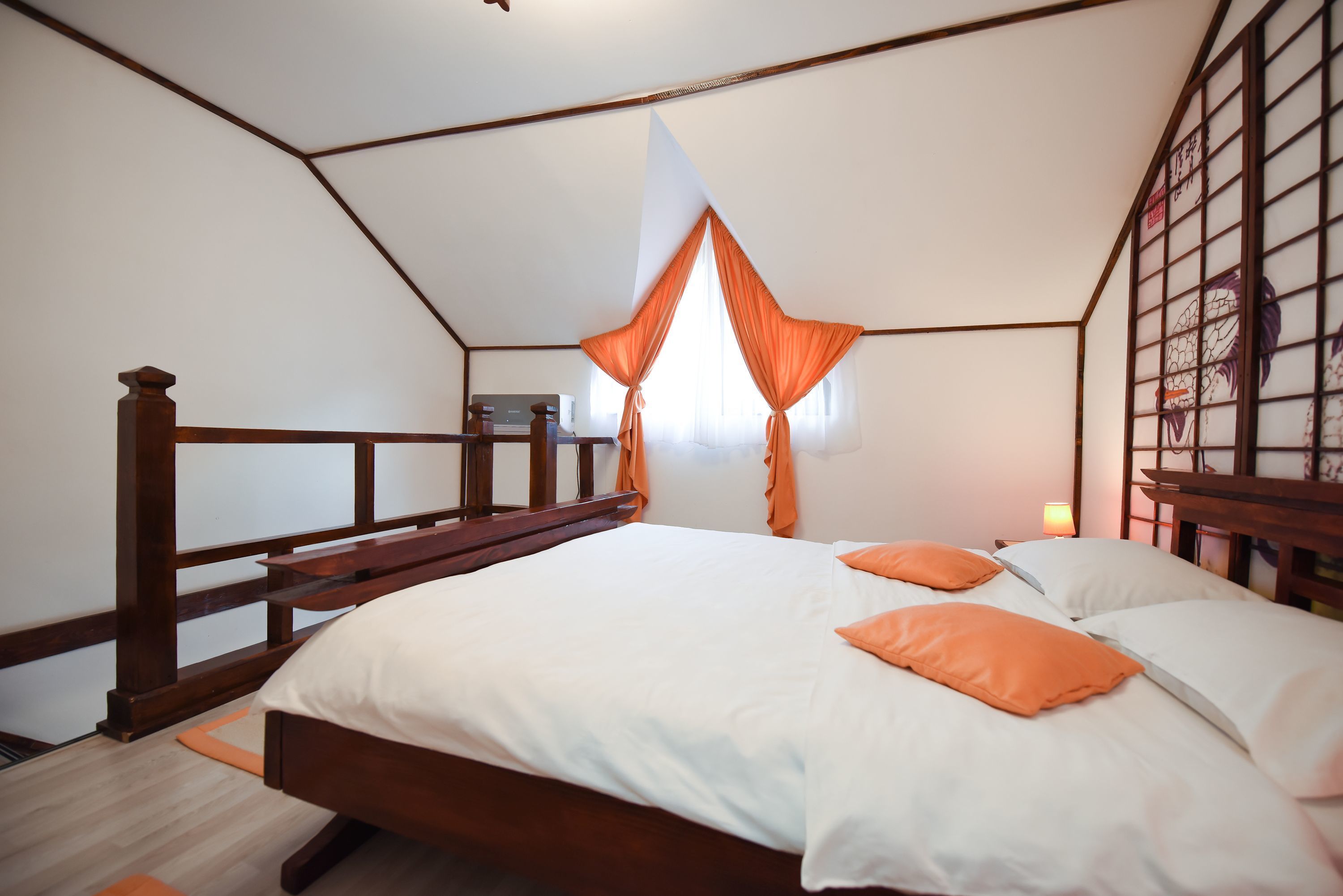 A bedroom with a wooden bed, white bedding, orange pillows, a wooden headboard, and a window with orange curtains.