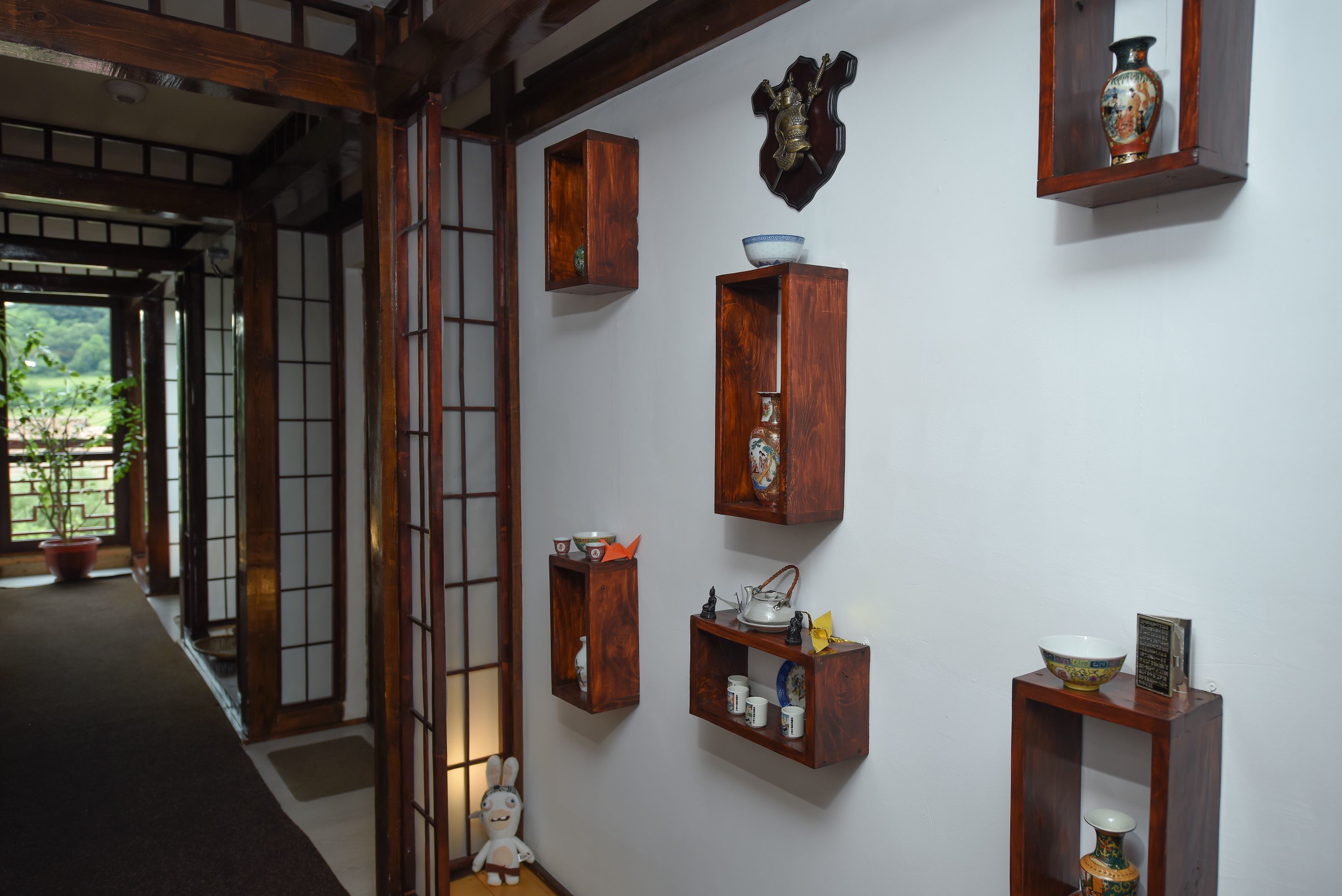 A traditional Japanese interior with wooden shelves displaying ceramics and a small figurine.