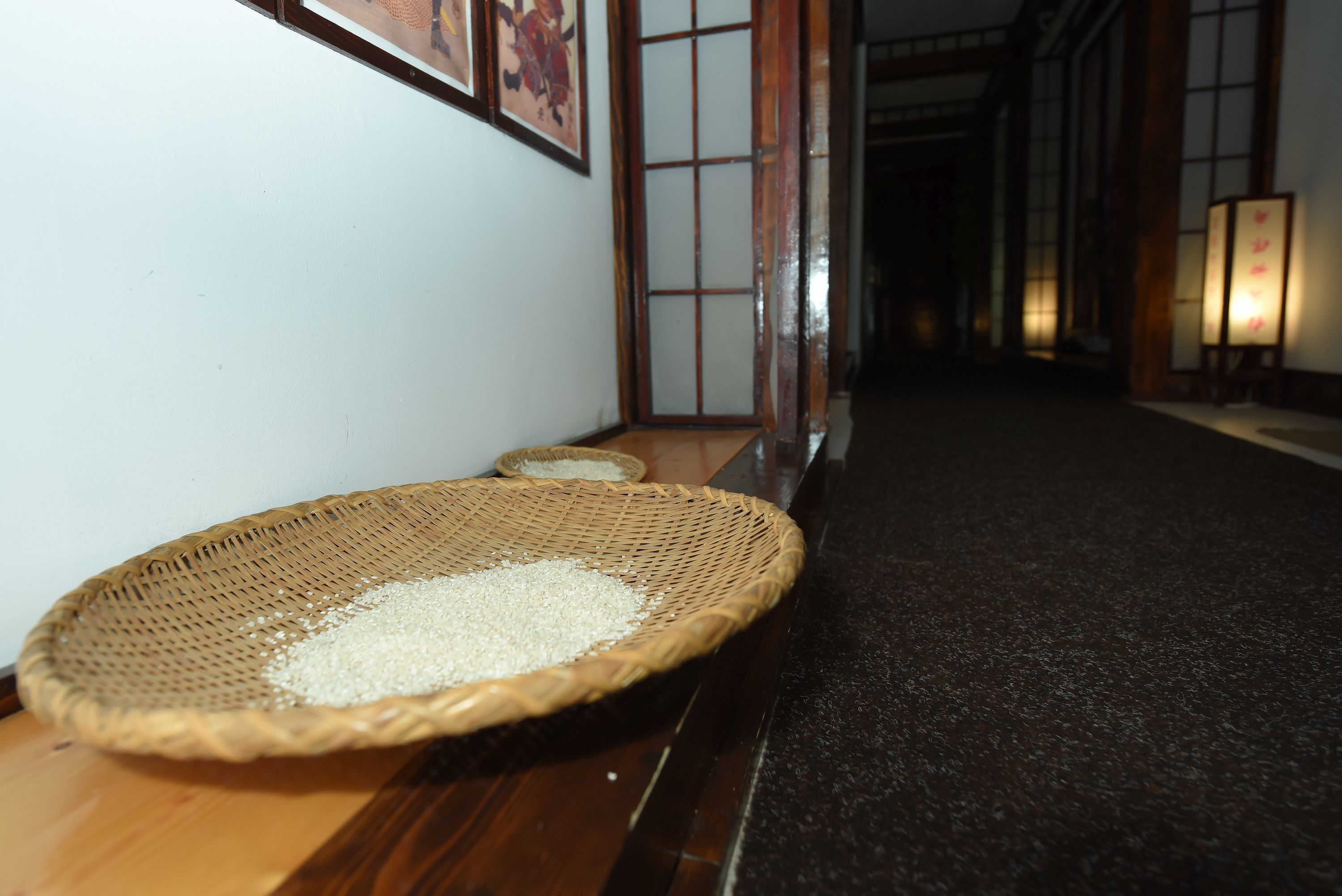 Un pasillo con piso de madera, una cesta tejida llena de granos y puertas correderas tradicionales japonesas.