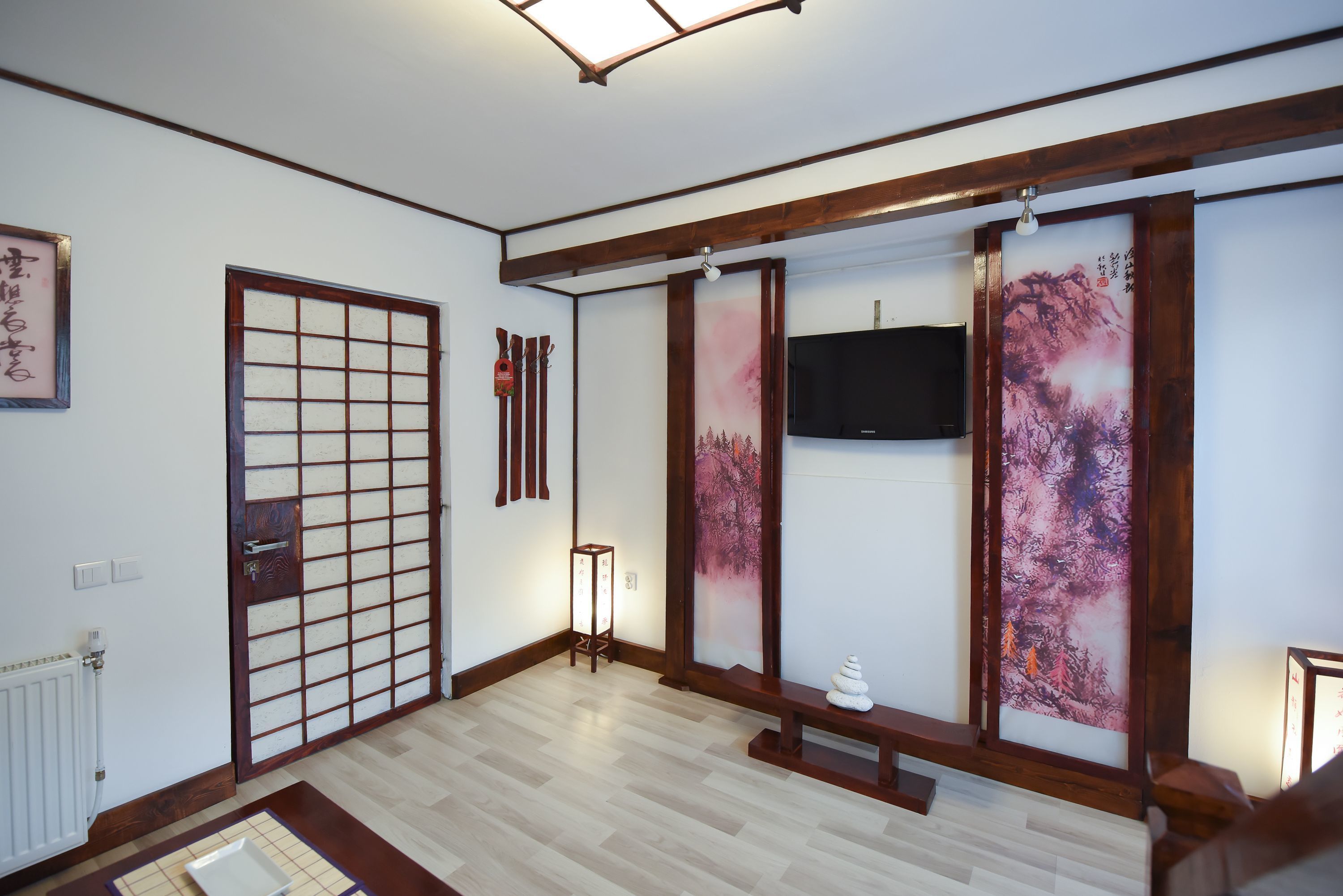 Ein traditioneller japanischer Raum mit Tatami-Böden, Shoji-Schirm, Wand-Fernseher und einem kleinen Tisch mit einem dekorativen Gegenstand.