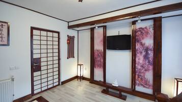 Ein traditioneller japanischer Raum mit Tatami-Böden, Shoji-Schirm, Wand-Fernseher und einem kleinen Tisch mit einem dekorativen Gegenstand.