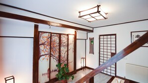 A traditional Japanese interior with tatami flooring, a shoji screen with cherry blossoms, a potted plant, and a low wooden table with chopsticks. - Casa Lily-Japanese Retreat (Sighisoara)