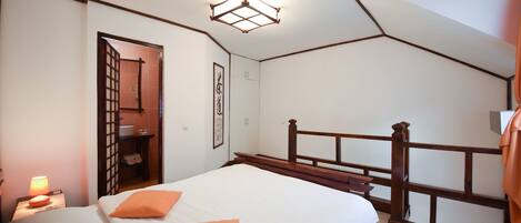Une chambre à coucher avec une tête de lit en bois, deux lits avec des oreillers orange, une table de chevet avec une lampe et un luminaire au plafond.