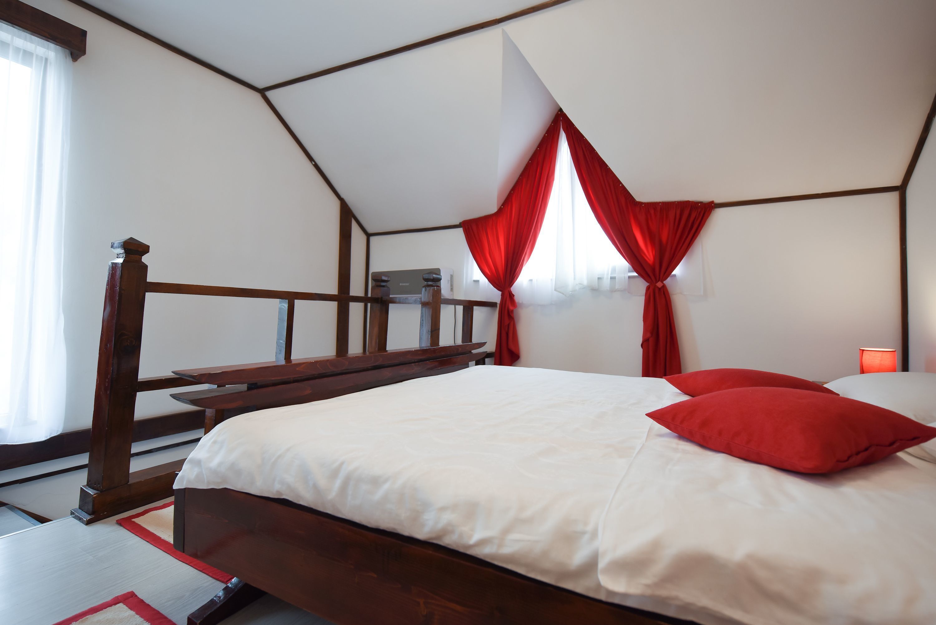 A bedroom with a wooden bed, white bedding, and red curtains.