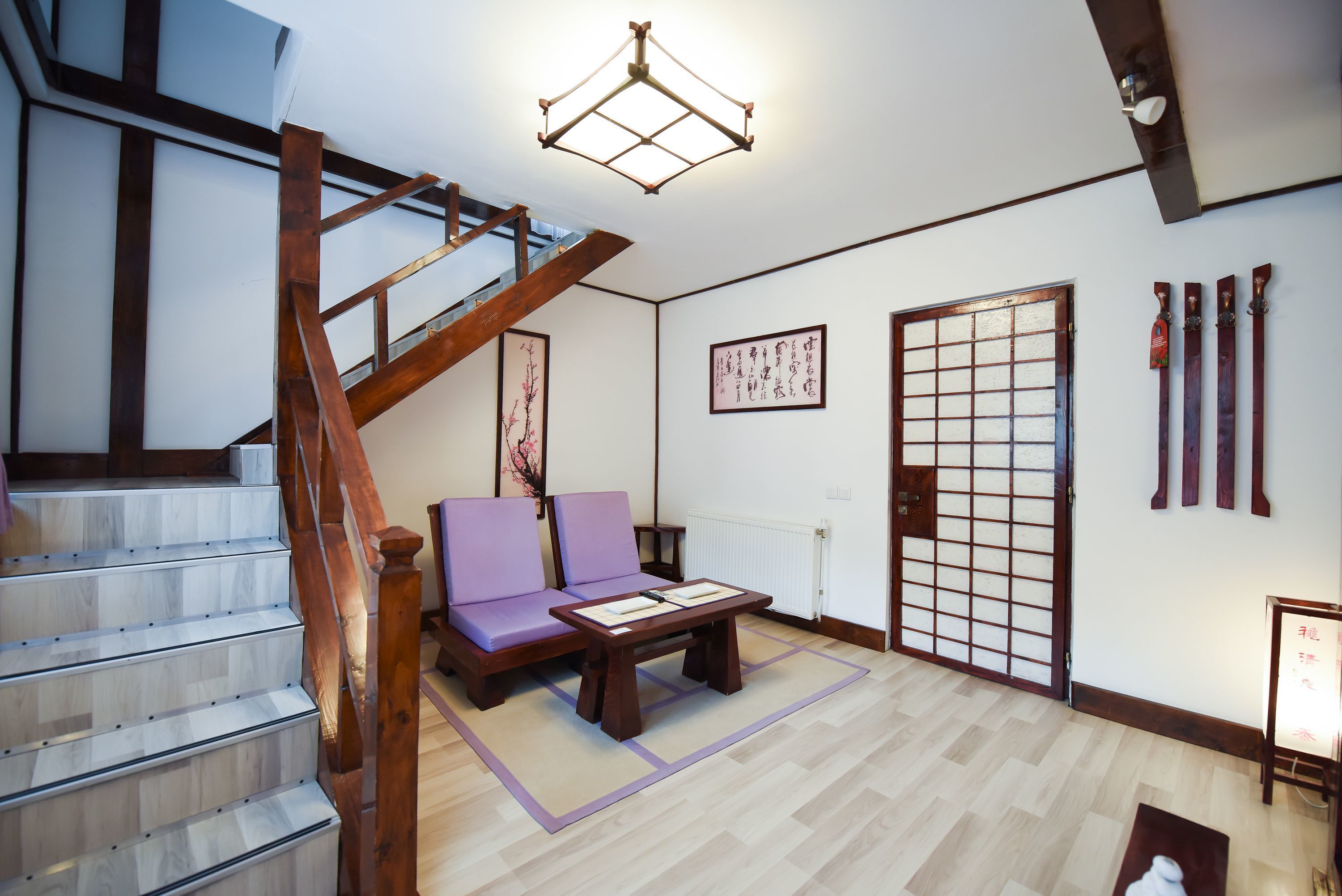 Una habitación de estilo japonés tradicional con suelo de tatami, una mesa de madera baja, un sofá morado, un divisor deslizante shoji y una escalera de madera.