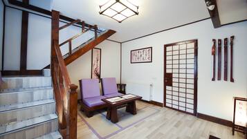 Una habitación de estilo japonés tradicional con suelo de tatami, una mesa de madera baja, un sofá morado, un divisor deslizante shoji y una escalera de madera.