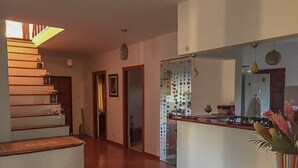 Un vaste espace de vie agrémenté d’un escalier en bois, une cuisine dotée d’un plan de travail blanc et un coin repas avec une nappe à rayures.
