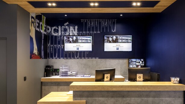 A reception desk with two HP monitors, a coffee machine, and a glass display case. - ibis budget Bilbao City (Bilbao)