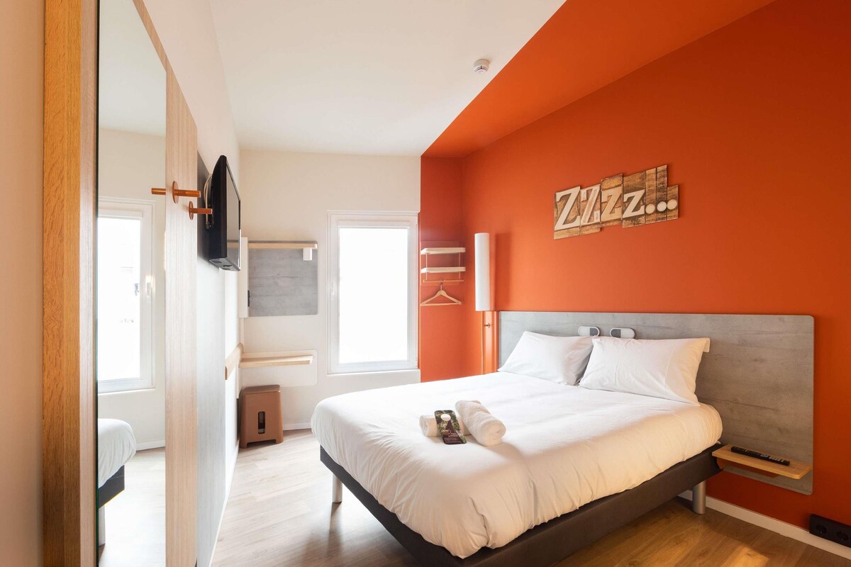 Un dormitorio moderno con una cama grande, un televisor montado en la pared y una pared de acento naranja brillante.