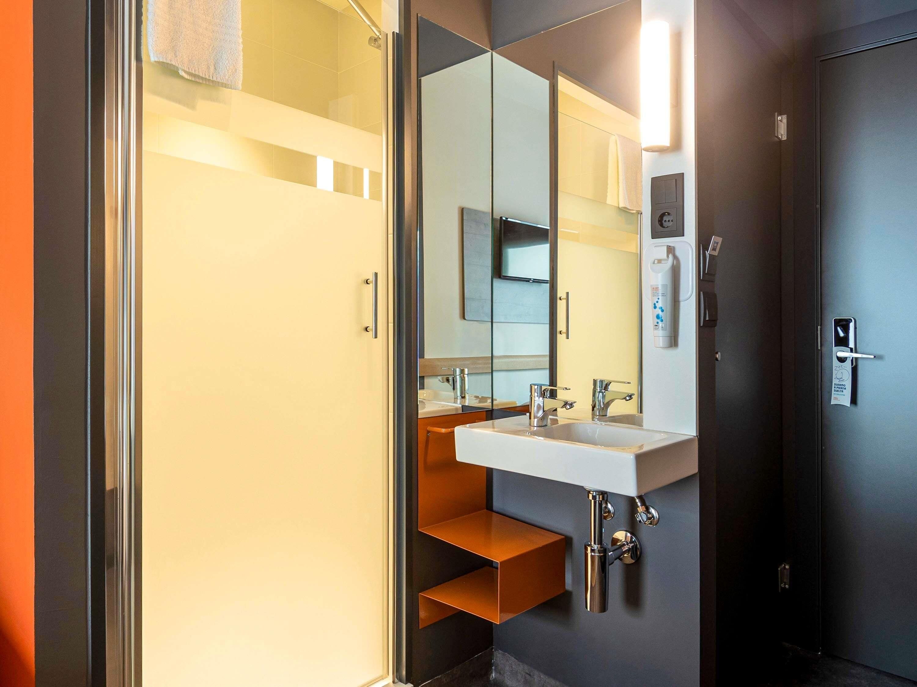 Een moderne badkamer met een douchecabine van glas, een witte wastafel en een grote spiegel.