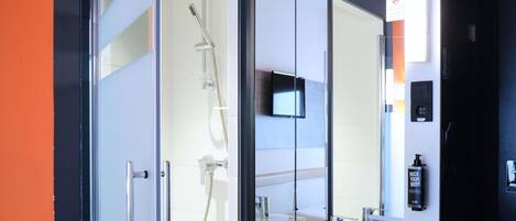 A modern bathroom with a glass shower enclosure, a white sink, and a mounted television.