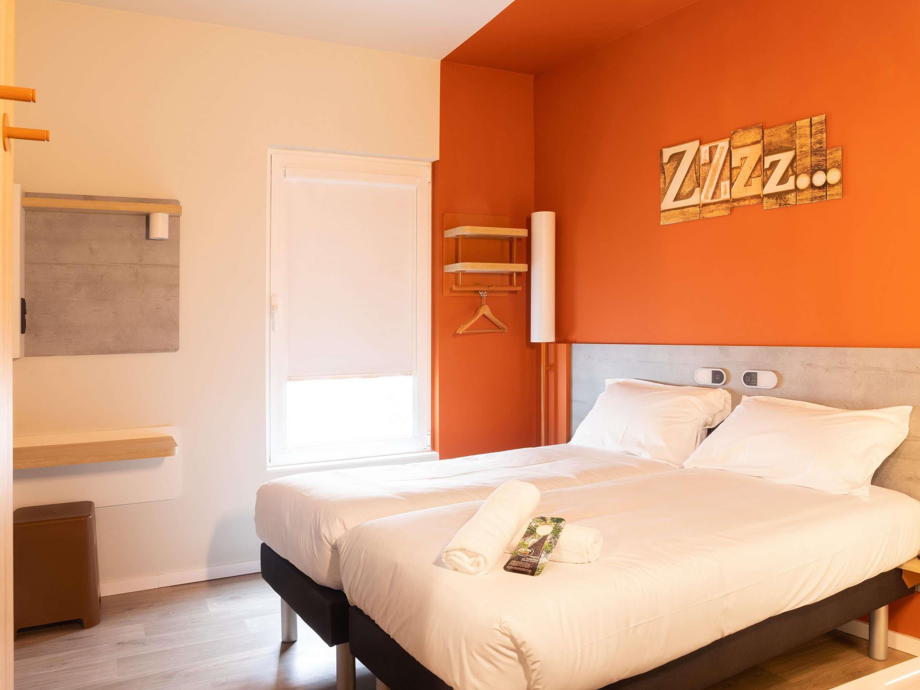 A bed with white linens, a towel, and a bottle of lotion on it.