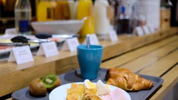 Bandeja de desayuno con croissant, jamón, huevos y un kiwi sobre una mesa de madera.