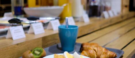 A breakfast tray with croissant, ham, eggs, and a kiwi on a wooden table.