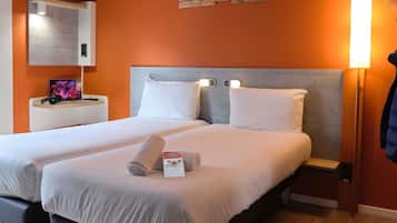 A hotel room with two beds, a desk with a laptop, a wall-mounted mirror, and a wall art piece.