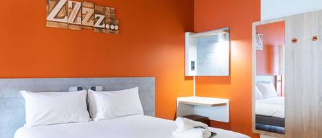 A hotel room with a large bed, a bedside table, a wall-mounted mirror, and a 'ZIZ' artwork.