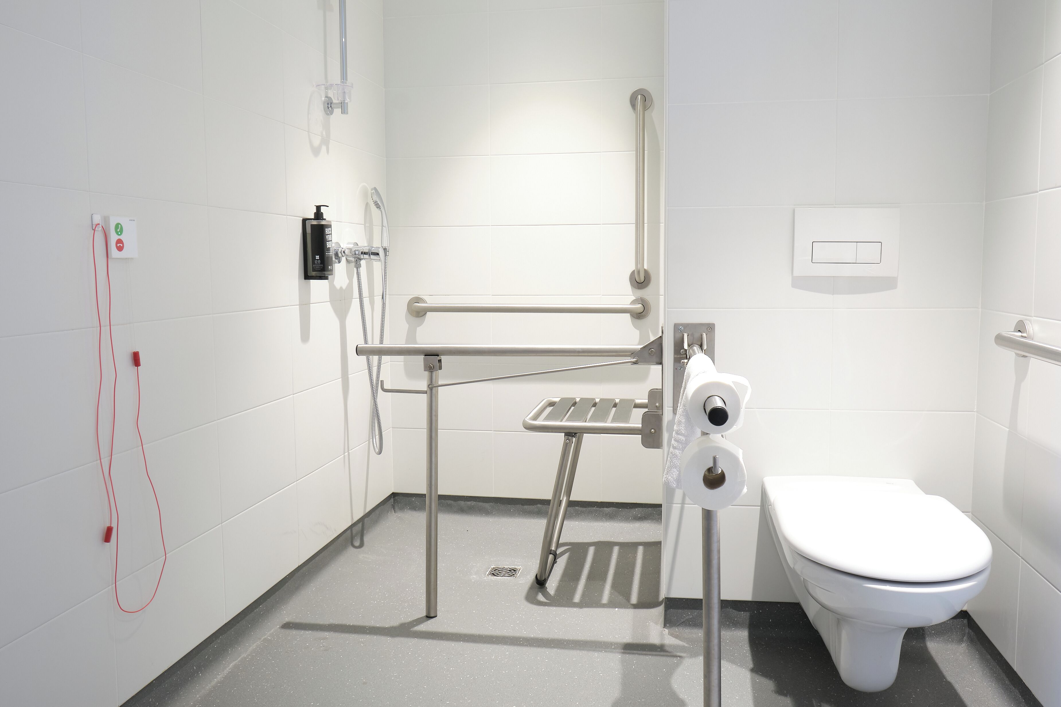 A modern bathroom with a white toilet, a hand dryer, and a grab bar.