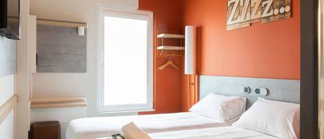 Habitación de hotel con dos camas, un armario, un espejo, una ventana y una pared decorada con la inscripción 'Zzz'.