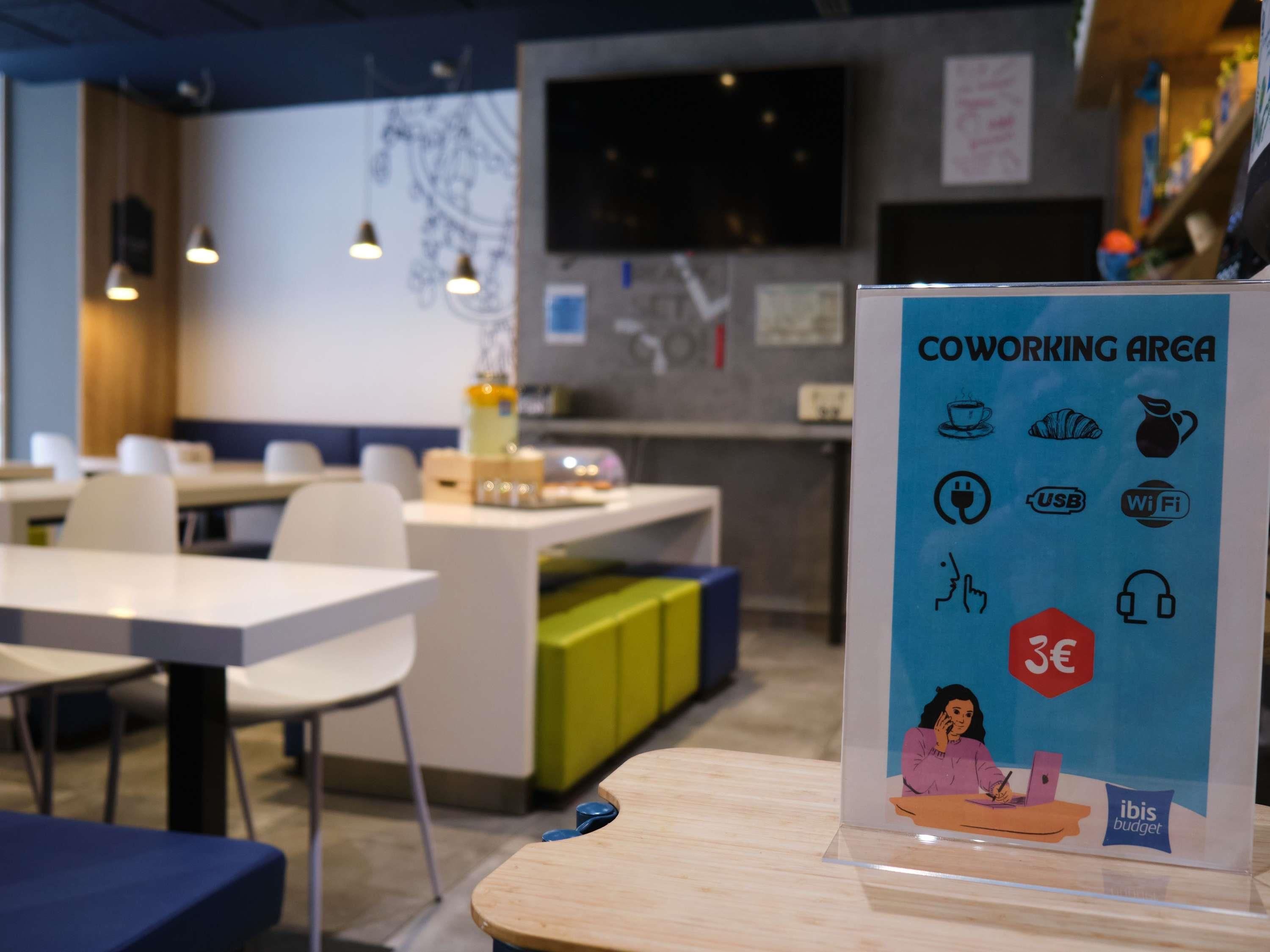 A coworking area with tables, chairs, and a sign indicating amenities like Wi-Fi, USB charging, and a 3€ coffee option.