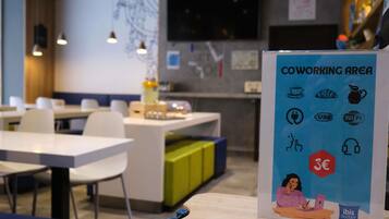 A coworking area with tables, chairs, and a sign indicating amenities like Wi-Fi, USB charging, and a 3€ coffee option.