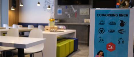 A coworking area with tables, chairs, and a sign indicating amenities like Wi-Fi, USB charging, and a 3€ coffee option.