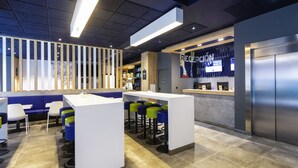 A modern reception area with a counter, seating, and a large screen displaying information. - ibis budget Bilbao City (Bilbao)