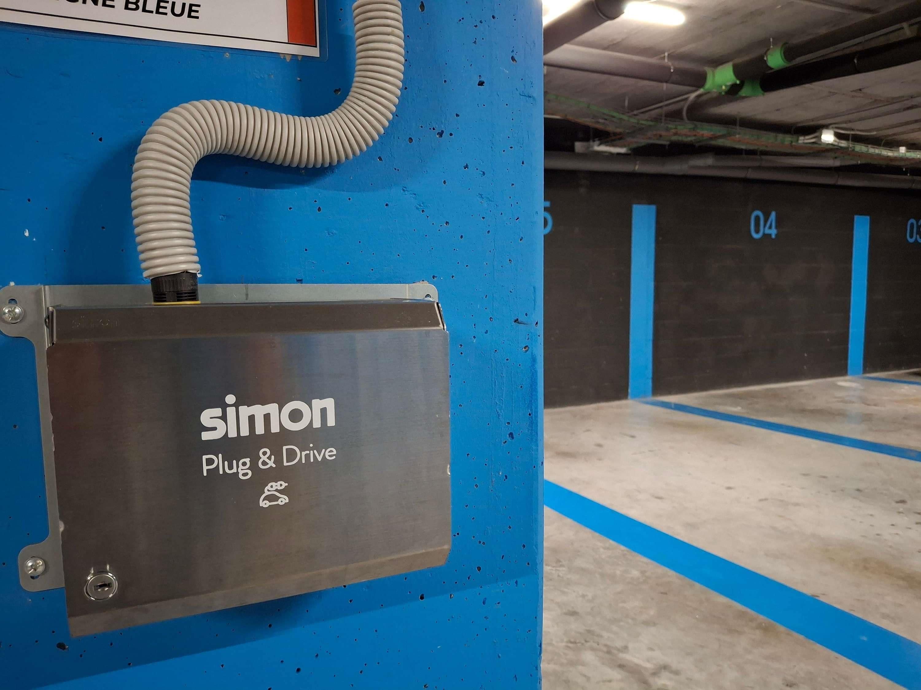 A parking garage with a blue wall and a sign that reads 'Simon Plug & Drive.'