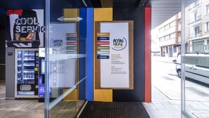 A hotel entrance with a vending machine, a bulletin board with various notices, and a glass door leading inside. - ibis budget Bilbao City (Bilbao)