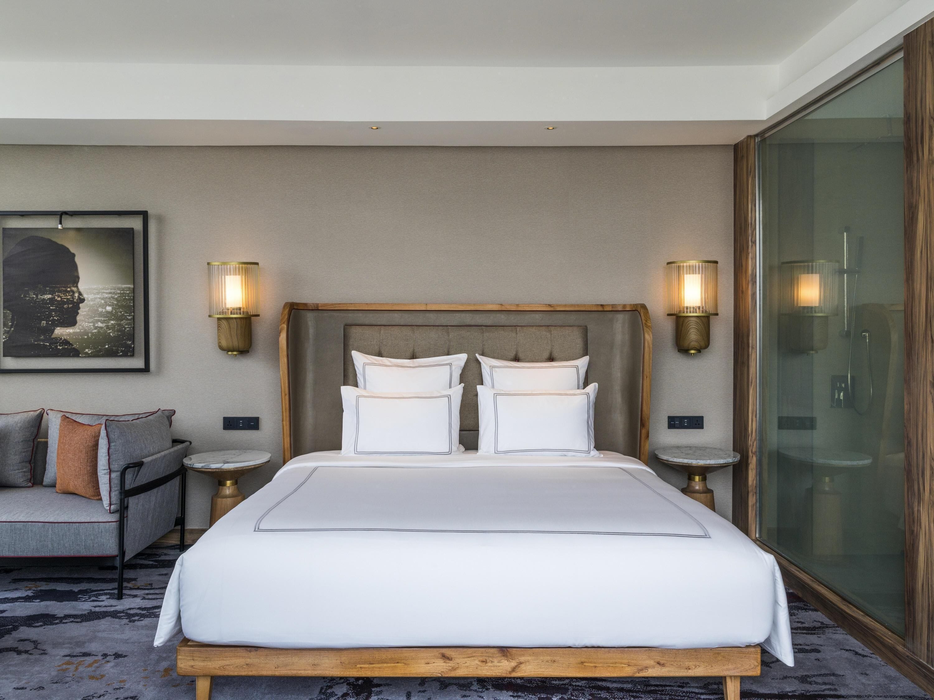 A hotel room with a large bed, two bedside tables, a sofa, and a large window.
