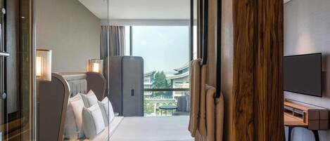 A modern hotel room with a large bed, a TV, and a view of the cityscape.