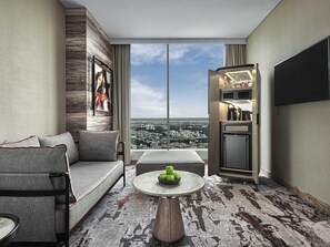 Ein modernes Wohnzimmer mit einer Couch, einem Couchtisch mit Äpfeln, einem Fernseher und Blick auf eine Stadtlandschaft.