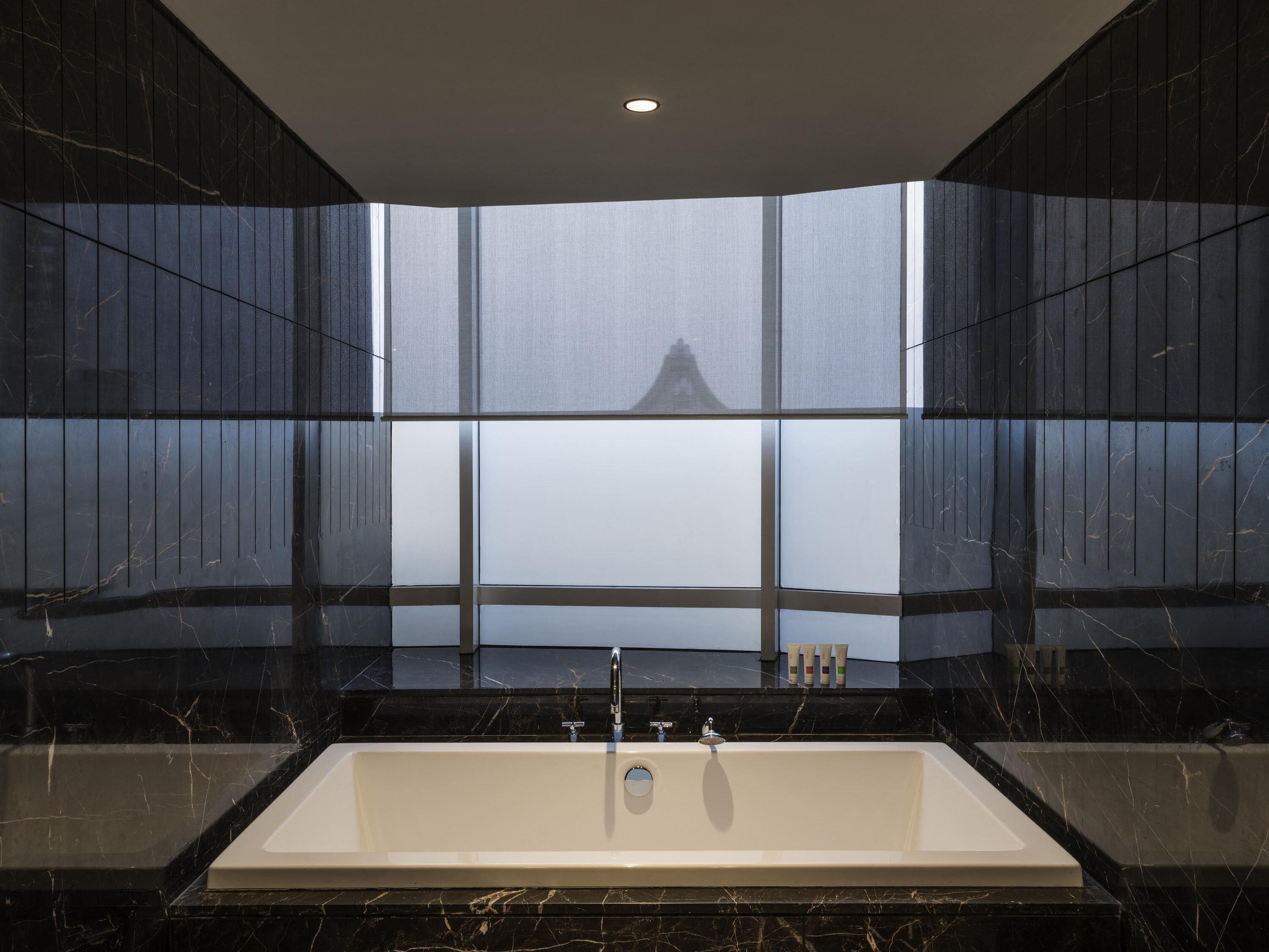 A modern bathroom with a large bathtub, dark marble walls, and a view of a traditional Japanese temple through large windows.