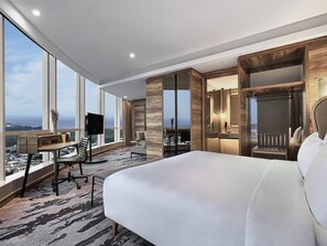 A modern hotel room with a large bed, a desk with a chair, a TV, and a view of the cityscape through large windows. - Swissôtel Jakarta PIK Avenue (Jakarta)