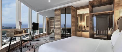 Habitación de hotel moderna con una cama grande, un escritorio con una silla, un televisor y vistas de la ciudad a través de amplias ventanas.