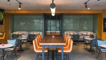 A modern dining area with a wooden table and orange chairs, surrounded by sofas and small tables.