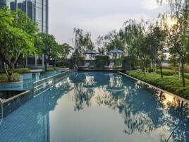 Una piscina con sillas de descanso y sombrillas, rodeada de vegetación y edificios modernos.