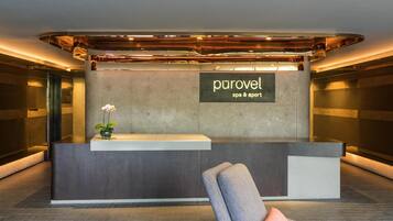 Un mostrador de recepción con un cartel que dice 'purovel spa & sport' en un vestíbulo moderno con una silla y un jarrón de flores.