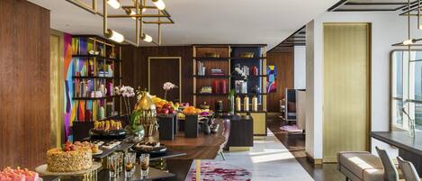 A modern hotel lobby with a central bar area, bookshelves, and a seating area with a view of the city.