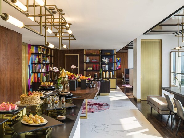 A modern hotel lobby with a central bar area, bookshelves, and a seating area with a view of the city.