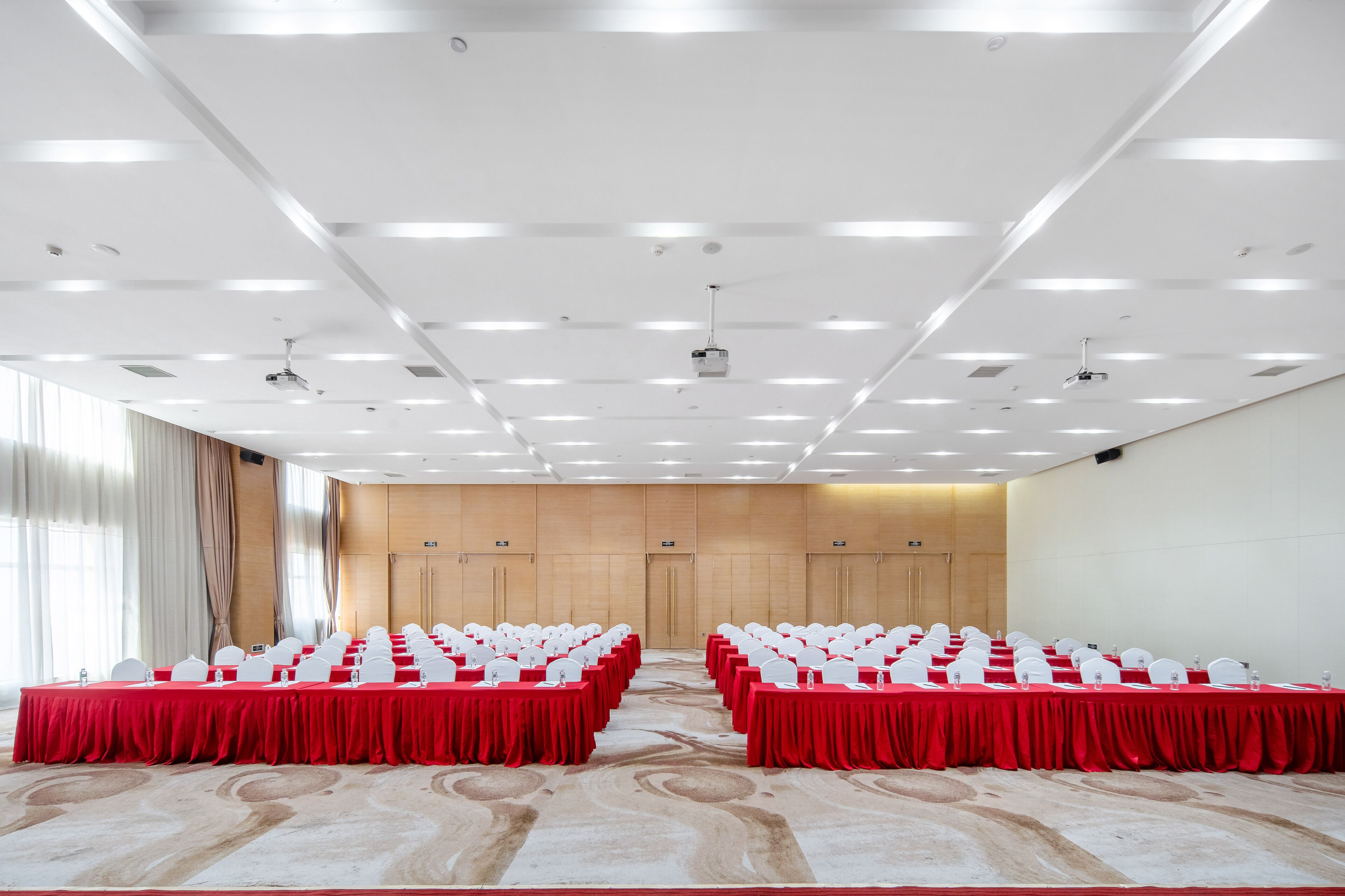 Un salón de conferencias con mesas y sillas dispuestas en filas, suelo alfombrado e iluminación empotrada en el techo.