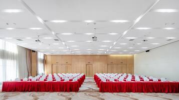 A conference room with rows of tables and chairs, a carpeted floor, and a ceiling with recessed lighting.
