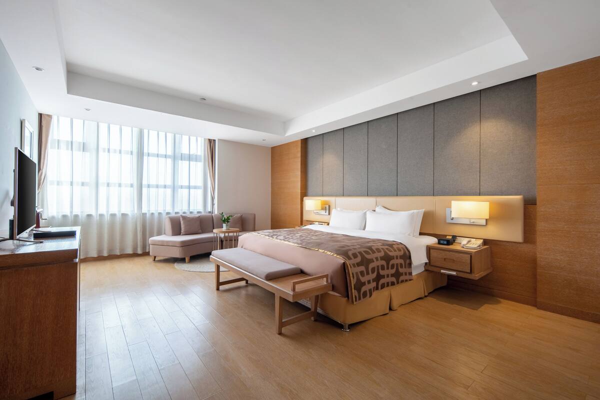 Ein modernes Hotelzimmer mit einem großen Bett, Nachttischen, einem Schreibtisch und einer Sitzecke.