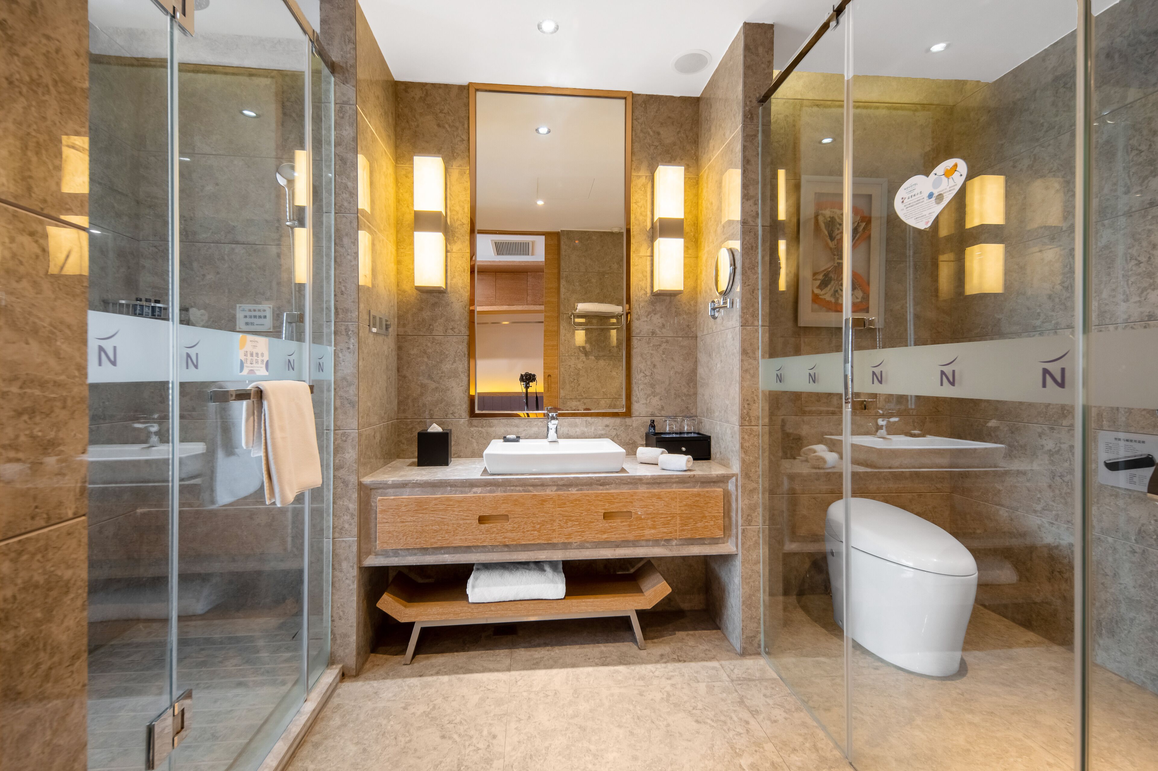 Een moderne badkamer met een douchecabine van glas, een houten wastafelmeubel en een wit toilet.