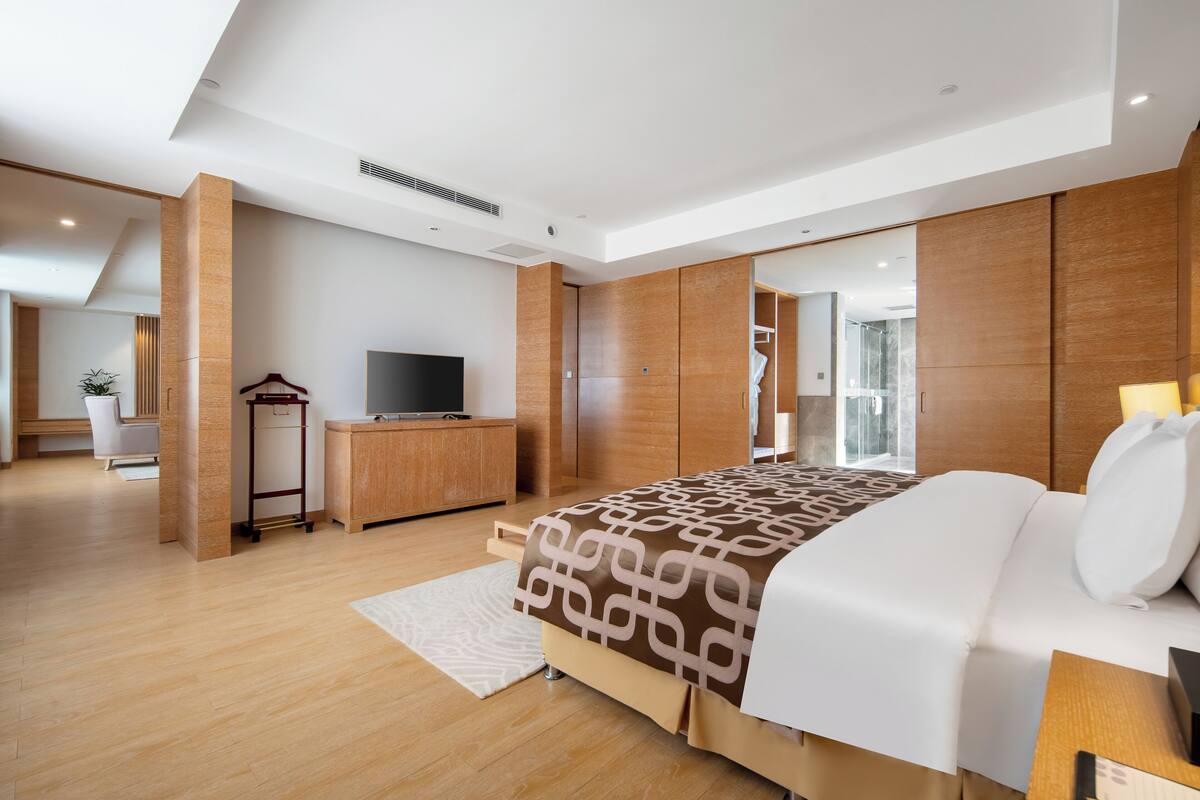 Ein modernes Hotelzimmer mit einem großen Bett, einem Schreibtisch mit Fernseher, Holzvertäfelung und Blick ins Freie.