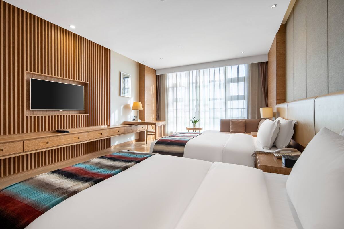 Ein Hotelzimmer mit zwei Betten, einem Fernseher, einem Schreibtisch und einem großen Fenster.